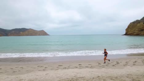 Atletas-Femeninas-De-Maratón-Corriendo-Una-Carrera-Hacia-El-Final-En-Una-Hermosa-Playa-A-Lo-Largo-De-Una-Costa-Azul-Y-El-Mar,-El-Dron-Vuela-Sobre-Ellas---Disparo-De-Dron---50fps