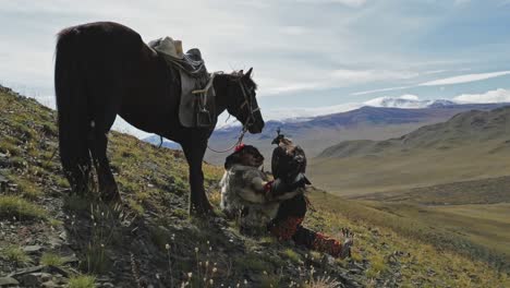 Golden-eagle-hunter-on-rocky-hillside-summit-with-Horse-and-Eagle,-in-Altai-Mountains