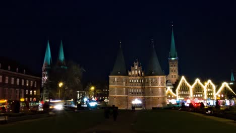 Lapso-De-Tiempo-De-Panorámica-De-La-Puerta-Occidental-Del-Museo-Holstentor-En-Lübeck,-Alemania,-Por-La-Noche-Con-Iglesias-Al-Fondo