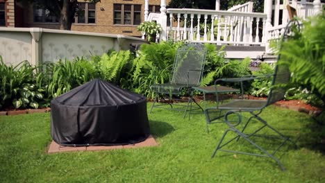 Shot-of-black,-outdoor-fire-place-and-lawn-furniture-in-a-backyard-surrounded-by-beautiful-ferns-and-a-swimming-pool