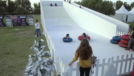 Una-Mujer-Mirando-A-Sus-Hijos-Mientras-Baja-Por-El-Tobogán-Blanco-En-El-Carnaval-De-Invierno-En-Abu-Dhabi,-Emiratos-Árabes-Unidos---Inclinada-Hacia-Arriba