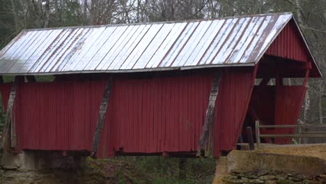 A-steady-shot-of-a-covered-bridge-in-the-rain-with-people-walking-into-it