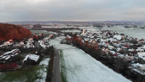Drone-flight-over-snowy-village-with-nearby-high-traffic-road