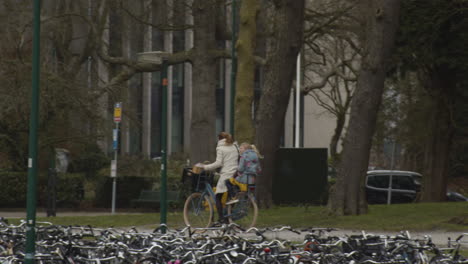 Mujer-En-Bicicleta-En-Un-Clima-Ventoso-Con-Su-Hija-En-El-Asiento-Trasero-De-La-Bicicleta