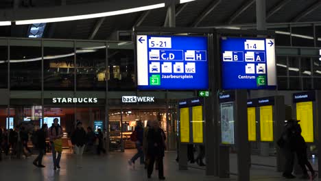 People-with-suitcases-walking-through-the-screen-in-a-train-station,-shops-in-the-background