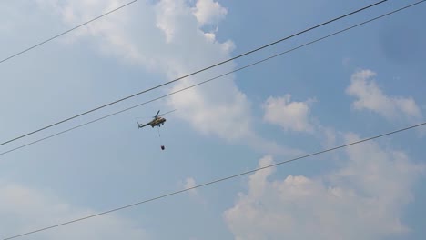 Ein-Armeehubschrauber-Transportiert-Wasser-Und-Fliegt-über-Eine-Große-Übertragungsleitung,-Um-Einen-Waldbrand-Zu-Löschen