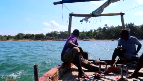 Three-tanzanian-men-sailing-a-wooden-motorboat-away-from-Fumba-village-at-noon