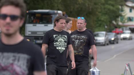 Metal-fans-dressed-in-black-walking-in-street-during-festival,-pointing-to-camera