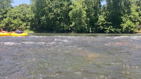 A-static-shot-of-a-couple-take-float-in-tubes-down-the-river-during-the-summer