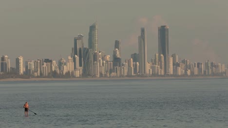 28-Jan-2023---People-surfing-at-Burleigh-Heads-at-sunrise-with-Surfers-Paradise-in-the-background-on-the-Gold-Coast,-Queensland,-Australia