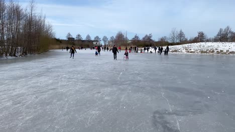 People-enjoy-ice-skating,-sledding-and-ice-walking-on-a-frozen-pond-in-a-city-park-in-the-Netherlands-in-2021