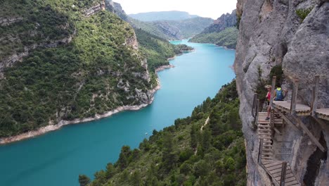 Pasarelas-de-Montfalco-at-Congost-de-Mont-Rebei-Canyon,-Catalonia-and-Aragon,-North-Spain---Aerial-Drone-View-of-Tourists-Walking-the-Dangerous-Stairs-along-the-Cliffs-and-Blue-River