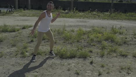 Talented-male-dancer-in-casual-wear-performing-on-sandy-road-while-moving-dynamically