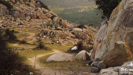 Young-man-riding-motorcycle-on-dirt-path-through-mountainside-rocky-wilderness