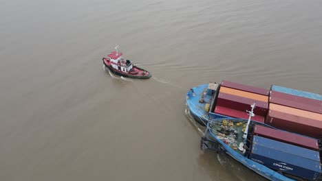 Aerial-view-of-large-container-ship-being-navigated-through-the-local-waters-by-small-vessel