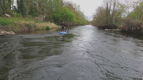 Paddleboard-POV:-Man-floats-narrow-river-riffles-in-rural-Ireland