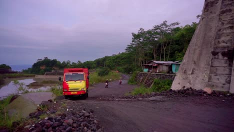 Close-up-shot-of-truck-and-motorcyclist-driving-on-rural-road-beside-sand-mine-lake-in-Indonesia