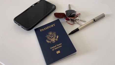 Pasaporte-4k-De-Los-Estados-Unidos-De-América-Sentado-En-Una-Cómoda-De-Escritorio-Con-Las-Llaves-Del-Auto-Y-Un-Teléfono-Mientras-La-Mano-Del-Hombre-Lo-Levanta