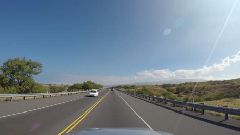 Driving-on-the-road-through-dry-grass-and-bush-landscape-in-Hawaii,-dash-cam-pov