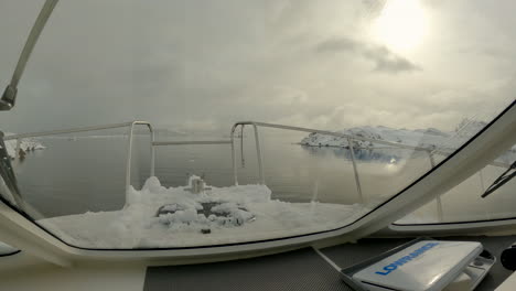 View-from-inside-the-cockpit-of-a-boating-as-it-cruises-over-very-calm-water-between-snow-covered-rocky-outcrops-of-an-inlet-in-Norway
