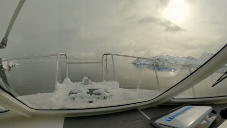 Blick-Aus-Dem-Cockpit-Eines-Bootes,-Das-über-Sehr-Ruhiges-Wasser-Zwischen-Schneebedeckten-Felsvorsprüngen-Einer-Bucht-In-Norwegen-Fährt