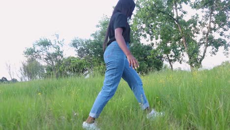 Low-angle-shot-of-a-girl-in-the-park-walking-through-the-grass,-gazing-off-to-the-distance-exploring-nature-Harare,-Zimbabwe
