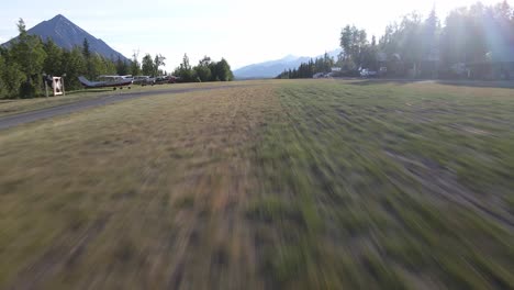 Drone-or-UAV-aerial-dolly-shot-of-a-takeoff-towards-sunset-from-a-private-grass-runway-in-a-remote-portion-of-the-Talkeetna-Range