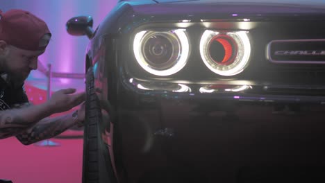 Dodge-Challenger-Sports-Car-Front,-Modern-Neon-Headlights-and-Letters-Logo-With-Man-Polishing-Wheels,-Slow-Motion-Dolly-Shot