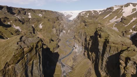 Aerial-landscape-view-of-a-mountain-canyon-with-a-river-flowing-from-melting-snow,-on-a-sunny-day-in-Iceland