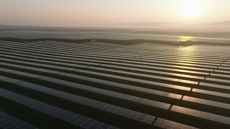 Sonnenaufgang-über-Einem-Riesigen-Solarpark-Mit-Reihen-Von-Sonnenkollektoren,-Die-Sich-Bis-Zum-Horizont-Erstrecken