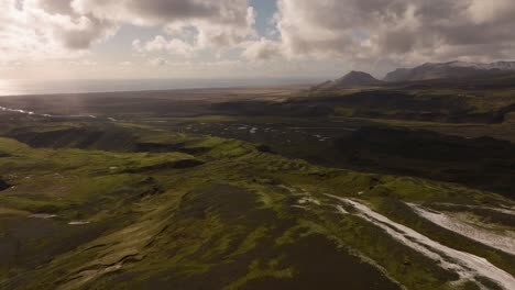 Aerial-view-of-the-expansive-green-and-snowy-landscape-of-Sólheimajökull,-featuring-rolling-hills-and-distant-mountains