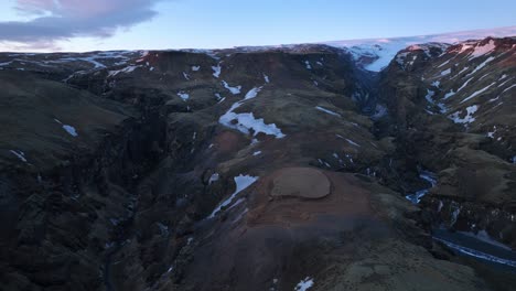 Aerial-panoramic-landscape-view-of-mountains-and-glacial-valleys-with-snow-melting-into-rivers,-in-Iceland-at-dusk