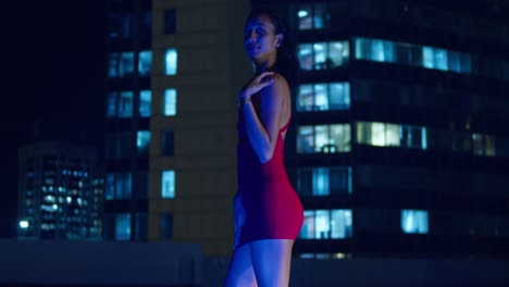 A-Hispanic-girl-stands-on-a-rooftop-with-the-Caribbean-city-lights-of-Port-of-Spain,-Trinidad-in-the-background