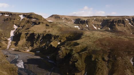 Aerial-panoramic-view-over-a-mountain-valley-with-a-river-flowing-from-melting-snow,-in-Iceland,-on-a-sunny-morning