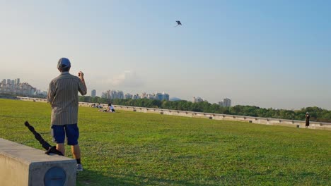 Vista-Trasera-Del-Hombre-Mayor-Volando-Cometa-En-El-Bombardeo-Del-Puerto-Deportivo-En-Un-Día-Soleado