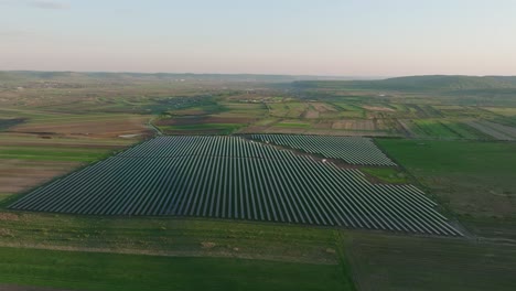 A-vast-solar-farm-stretches-across-a-rural-landscape-during-sunset,-aerial-view