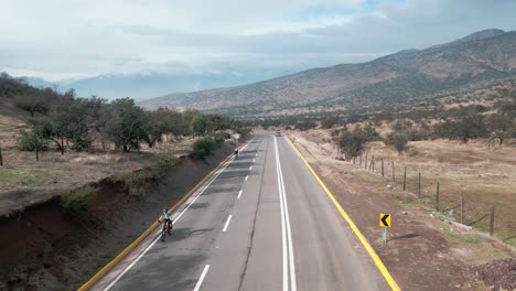 Ciclistas-Por-La-Avenida-Principal,-Cerca-De-Un-Cerro-En-El-Municipio-De-Barnechea,-Chile.