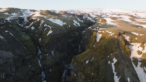 Aerial-landscape-view-over-a-mountain-canyon-with-melting-snow-and-a-river-flowing-inside