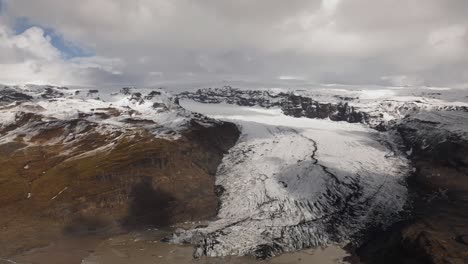 Aerial-hyperlapse-of-Sólheimajökull-Glacier-in-Iceland,-showcasing-the-expansive-ice-formations-and-surrounding-mountainous-landscape-with-fast-moving-clouds