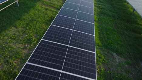Solar-panels-on-a-green-field-under-bright-sunlight,-aerial-view