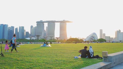 Marina-Barrage-Urban-Park-With-Sunrise,-Tracking-Shot-Capturing-People-Picnic-And-Hangout-On-The-Green-Grass-With-Cityscape-of-Marina-Bay-Sand-Singapore