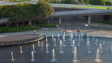 Vista-Superior-De-Pequeñas-Fuentes-En-El-Lago-En-El-Parque-De-La-Ciudad-Con-Gente-Corriendo-Y-Andando-En-Bicicleta-Por-La-Mañana