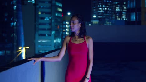 A-Hispanic-girl-on-a-rooftop-with-the-lights-of-Port-of-Spain,-Trinidad-illuminating-the-Caribbean-background