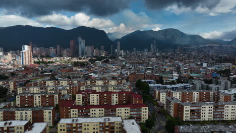 Drone-rising-over-condos,-toward-the-Bogota-skyline,-in-partly-sunny-Colombia