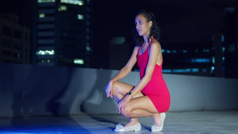 A-Hispanic-girl-is-on-a-rooftop,-with-the-city-lights-of-Port-of-Spain,-Trinidad-glowing-in-the-Caribbean-night-behind-her