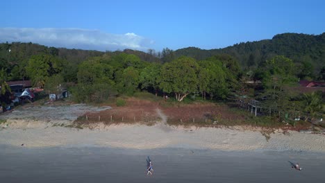 Tourists-enjoying-walking-on-the-beach-at-sunset-with-lush-green-tropical-forest-in-the-background