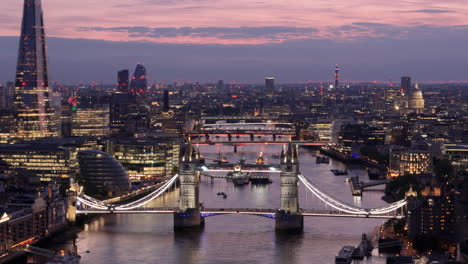 Illuminated-bridges-in-London-spanning-Thames-and-blue-hour-cityscape,-aerial