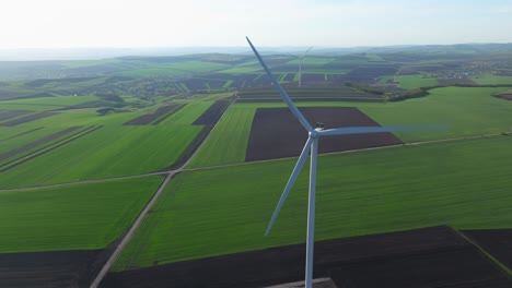 Wind-turbine-spinning-over-vast-green-and-brown-fields,-aerial-view