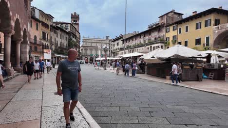 Piazza-delle-Erbe-filled-with-people-and-market-stools-in-Verona,-Italy