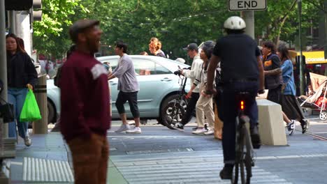 Un-Bullicioso-Paso-De-Peatones-Lleno-De-Peatones-Que-Cruzan-La-Calle,-Ciclistas-Que-Viajan-En-El-Carril-Bici,-Capturan-La-Vibrante-Vida-Urbana-De-La-Ciudad-De-Melbourne,-El-Distrito-Central-De-Negocios